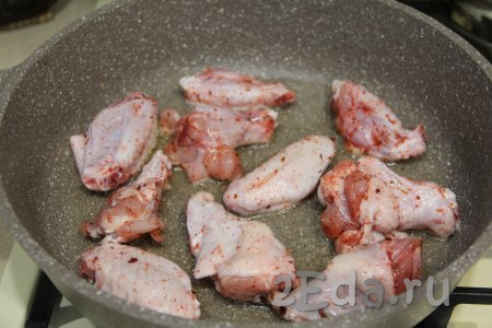 В сковороду с высокими бортиками влить масло, хорошо разогреть, а затем выложить куриные крылышки.