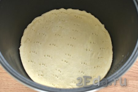 На круглой заготовке для пиццы делаем проколы вилкой, чтобы тесто не вздулось во время выпечки в мультиварке. Дно съёмной чаши мультиварки смазываем растительным маслом, выкладываем круг из слоёного теста.
