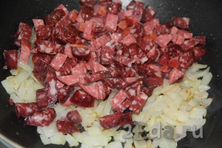 Колбасу (или колбаски) нарезать на средние кусочки и добавить в сковороду к луку, перемешать и обжарить пару минут.