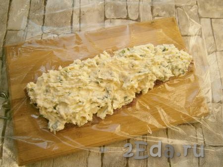 Одну часть филе сельди разместить на пищевой пленке и выложить сверху начинку из сыра и масла.