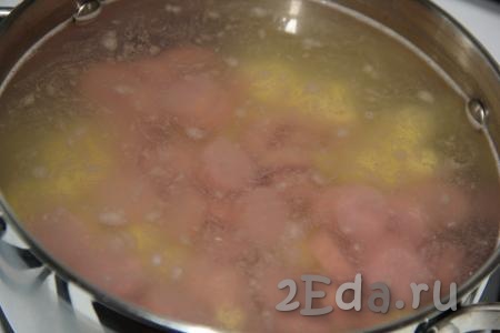 В кастрюлю влить 2 литра воды. Довести воду до кипения и добавить в кастрюлю нарезанные картофель и сосиски.