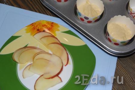 Яблоки вымыть и нарезать тонкими ломтиками. Чистить яблоки не нужно. Ломтики яблок запечь в течение 1-2 минут в микроволновой печи, чтобы они стали мягкими. Тесто выложить в формы, заполняя их на 1/2 объёма.